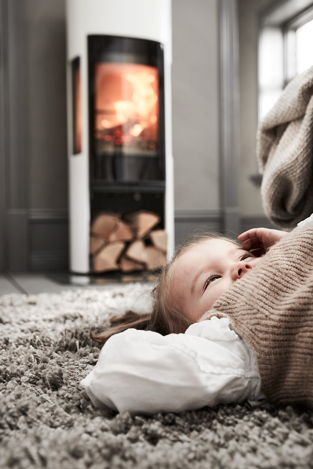A small child laying on a rug infront of a burning wood stove